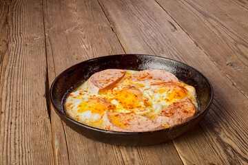 Fried eggs with sausage in a frying pan on a wooden table.