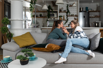 Happy married homosexual female gay couple laughing and embracing on the sofa with smile on their faces. Lesbian couple at home enjoying life together in their new apartment.