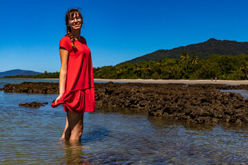 beautiful girl in red dress stands in coral reef water in daintree national park, vacation in queensland, australia; daintree rainforest