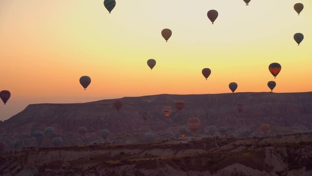 Balloons against backdrop of mountains and pink sky without clouds ea dawn. Balloons in sky in Cappadocia in Turkey. many small balloons flying in sky at dawn.