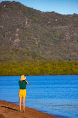 photographer girl in hat walks along paradise beach on magnetic island at sunset; recreation on magnetic island, queensland, australia