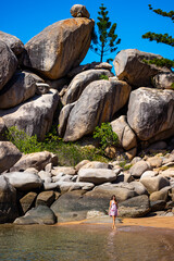 a beautiful long-haired girl in a dress relaxes on a paradise beach on magnetic island; a beach with massive rocks and turquoise water; relaxing on magnetic island, queensland, australia