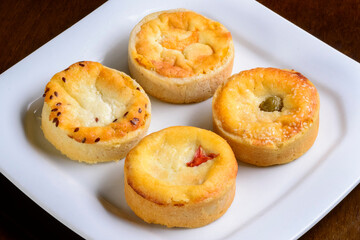 Mini quiches snacks of assorted flavors on a white plate.