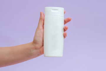 Woman holds a white bottle (cream, lotion, gel, shampoo) for cosmetic products isolated on lilac background