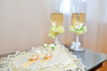 Two gold wedding rings on pillow with glasses of champagne