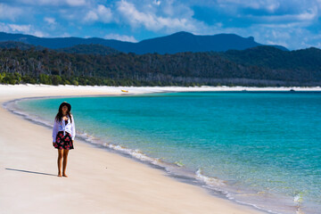 beautiful girl in dress and shirt and hat walks on paradise beach with white sand and turquoise water; walk on whitehaven beach on whitsunday island in queensland; paradise beaches of australia; sunny