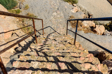 Escalera de piedra marrón con barandilla de metal, con arena de playa en exterior
