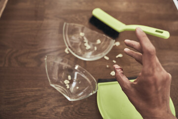 A wound with blood received when cleaning broken dishes. Close-up of a woman's finger on the background of a split cup and a brush with a dustpan for cleaning. High quality photo