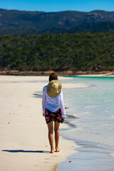 a beautiful girl in a dress, shirt and hat enjoys a walk on the white dunes at whitehaven beach; paradise beach with white sand and turquoise waters; whistundays island holiday, queensland, australia;
