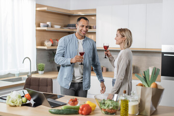 Happy multinational couple having fun while cooking healthy vegetarian meal in kitchen of their studio apartment. Wife and husband leading active lifestyle, enjoying life, spending time together.