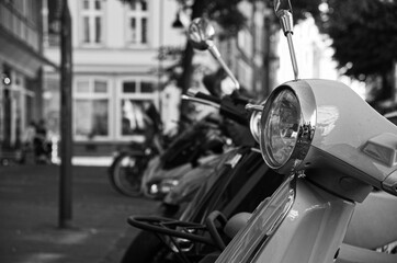 Grayscale partial view of motorcycles parked by a sidewalk