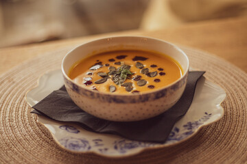 Pumpkin puree soup on a wooden background. Autumn cream soup decorated with pumpkin seeds and basil.