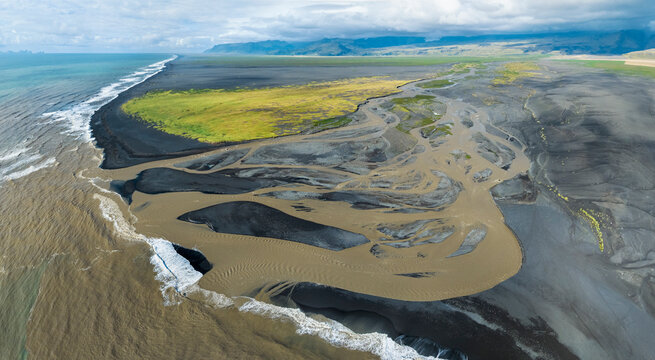 Aerial panorama of glacial river Jokulsa flowing into the sea with black beaches, south Iceland.