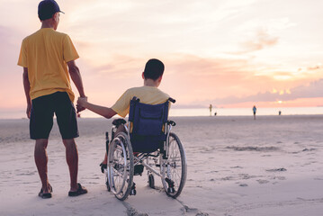 Behind of young man with disability holding hand father or volunteer or caregiver on the sea beach...