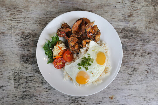 Fried Danggit with sunny egg and rice with tomato with salad served in dish isolated on wooden background top view of breakfast