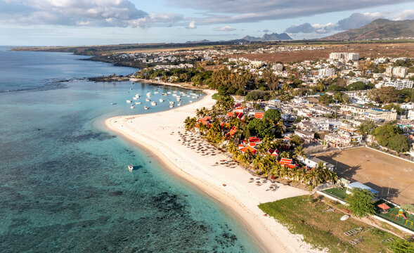 Panoramic aerial view a coastline with anchored boats, town, hotels and mountains in the background, Flic en Flac, Mauritius.