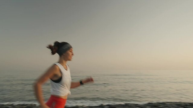 young woman enjoying a run in a pebbly beach at the sunset