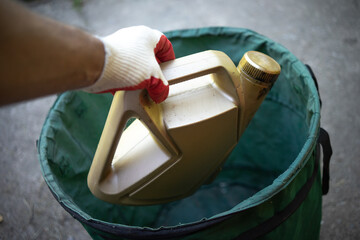 A gloved hand throws out a bottle of engine oil. Disposal of harmful mechanical engineering waste....