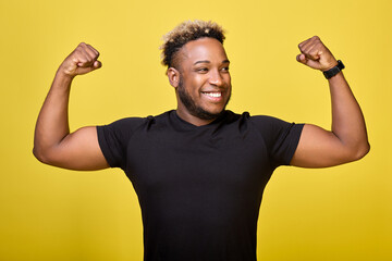 An African American smiling guy in a casual black T-shirt shows his physical strength. A confident,...