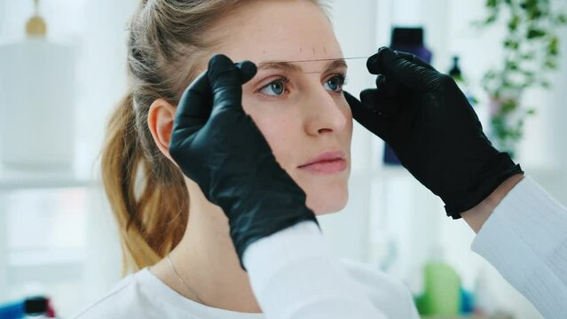 Cosmetologist marks the lines with a special thread to create the correct shape of the eyebrows during permanent makeup process