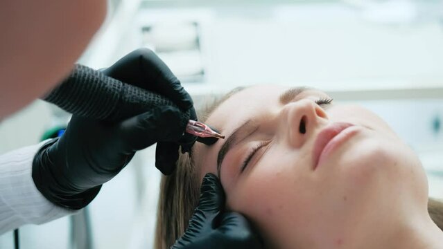 Cosmetologist finishing permanent makeup on second eyebrow of model