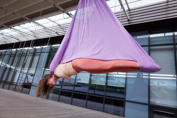 Sporty woman doing aero yoga in hammock. Brunette girl in sportswear exercising aerial yoga on...