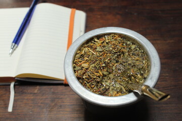 Yerba mate en una mesa de madera junto a un cuaderno con lapiceras en un lugar de trabajo típico de la cultura Argentina y de los gauchos. También correspondiente a la cultura de Paraguay y Uruguay © Teo 