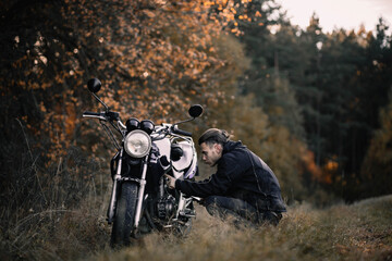 male motorcyclist repairs a motorcycle on the road outside the city in the forest.