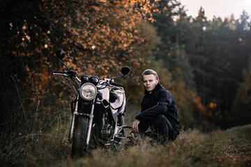 male biker motorcyclist with retro motorcycle in autumn forest.