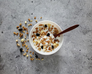 Baked muesli with yogurt, wooden spoon in white bowl on light background, top view.