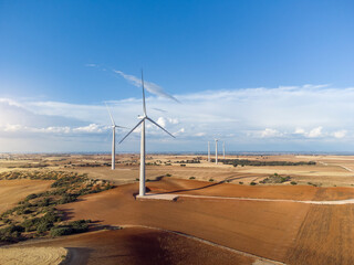 Aerial photograph of a field of windmills in a plowed crop field at sunset