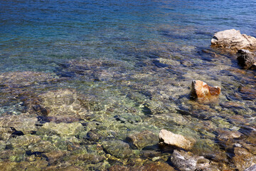 Transparent sea surface with stones on a bottom. Rocky beach, turquoise water for background