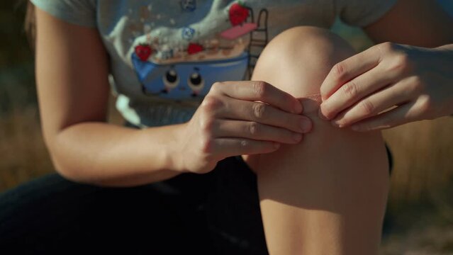 Close up of girl putting band-aid on knee after injury, fall, illness, protect wound. Concept of health and healthcare, physical recovery, outdoor sports.