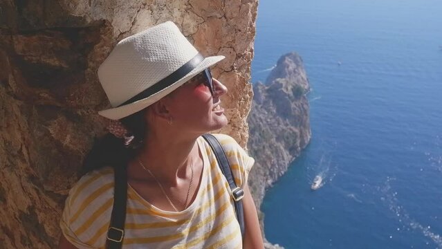 A woman tourist with a backpack and a hat sits on the fortress wall in the fortress of Alanya, Turkey. Beautiful sea landscape with a fortress.