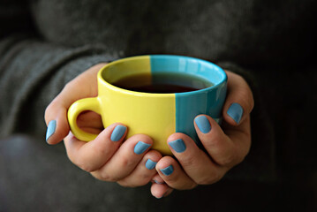 A mug in the colors of the Ukrainian flag in hands.