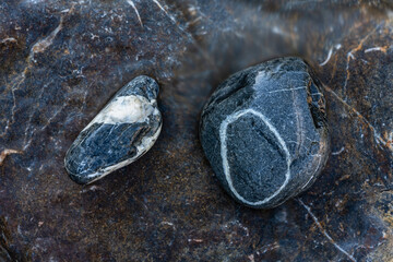 Two single black stones in a wet riverbed
