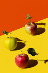 Red, green and red-green apple on a yellow and orange paper background