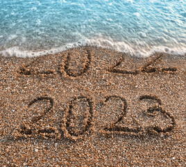 Handwritten inscription 2022 and 2023 on beautiful golden sand beach.