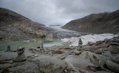 Rhone glacier and lake in the Swiss alps on a cloudy day in autumn with rock formations in the foreground
