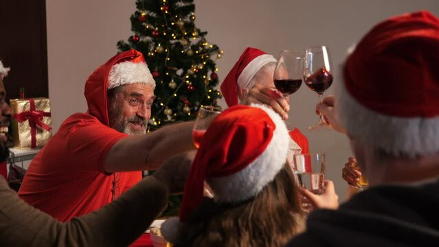 Group Of Diverse Family Gathering Enjoying With Christmas Celebration At Home, Happy People Clinking Glasses Together Eating Food Singing Song And Dancing Together In The Dining Room