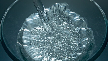 Naklejka na ściany i meble Sparkling aqua pouring glass top view closeup. Mineral drink filling glassware