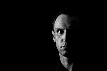 A black and white photograph of a middle-aged man showing strong emotions. A man in a black shirt on a dark background with a serious look.