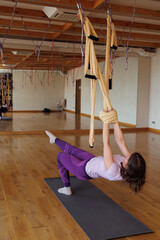 Young woman in sportswear practices different inversion aerial yoga with a hammock in beige hall....