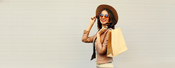 Portrait of beautiful happy smiling woman with shopping bags wearing jacket, round hat on gray background