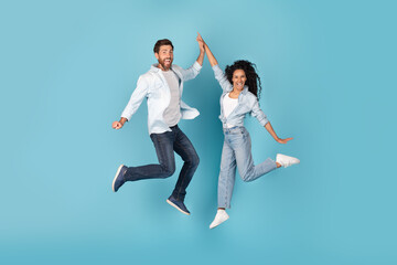 Fototapeta na wymiar Excited cheerful millennial caucasian and arabic couple jumping in air, give high five, on free space