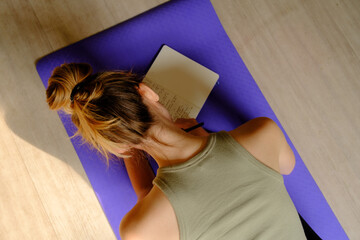 Overhead image of Young caucasian woman making a journal entry while sitting on a yoga mat.