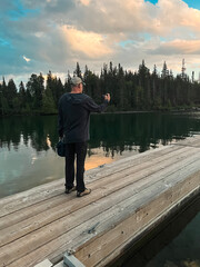 Man Standing on Wooden Pier Taking Picture on Phone of Stunning Scenery