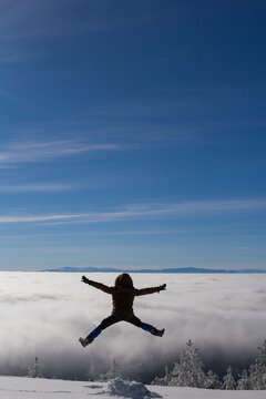 Vertical Shot Of A Male From Behind Jumping And Enjoying The View In Snowy Mountains