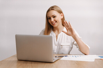 A young happy European woman using a laptop, waving, talking, holding a virtual meeting via remote video call or remote online interview, participating in a training webinar via video link