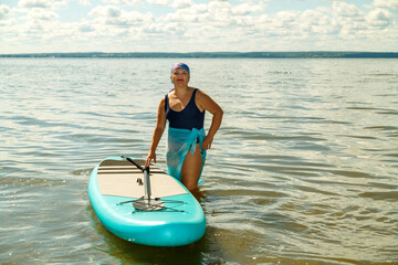 A woman is standing at the sapboard on the shore preparing for swimming.